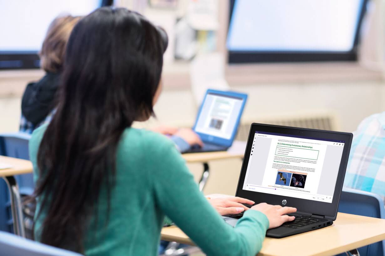 Two students sit at desks while typing on Chromebooks.