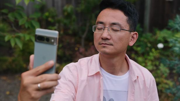 An Asian man with his eyes closed holding up a Pixel phone to take a selfie