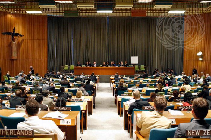 A wide view of the Trusteeship Council chamber with attendees sitting behind placards with country names at their seats.