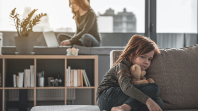 kid feeling lonely in foreground while mom works on laptop in background