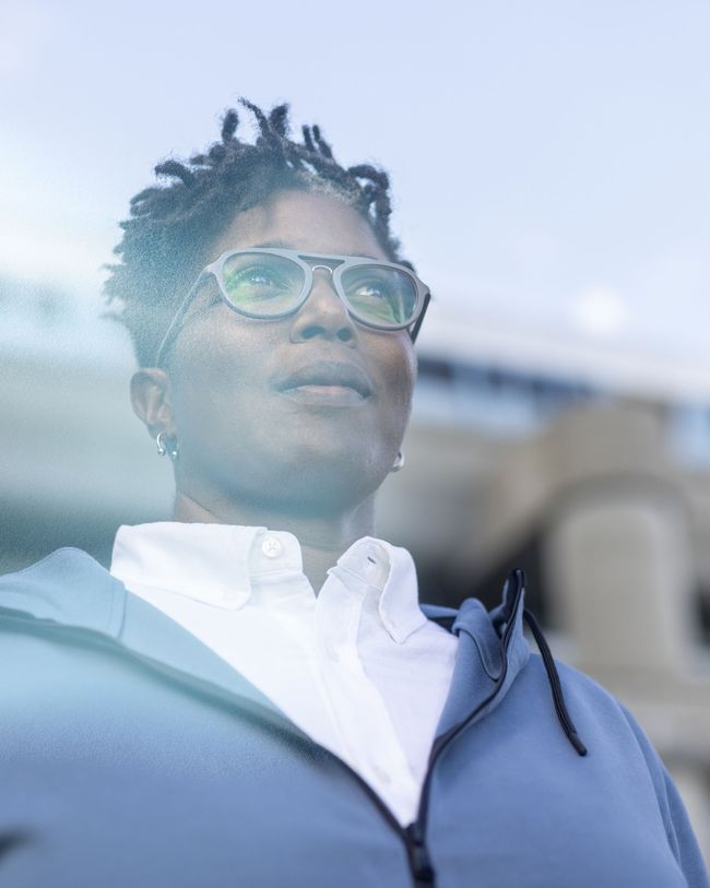 a woman wearing glasses and a blue jacket looks out a window