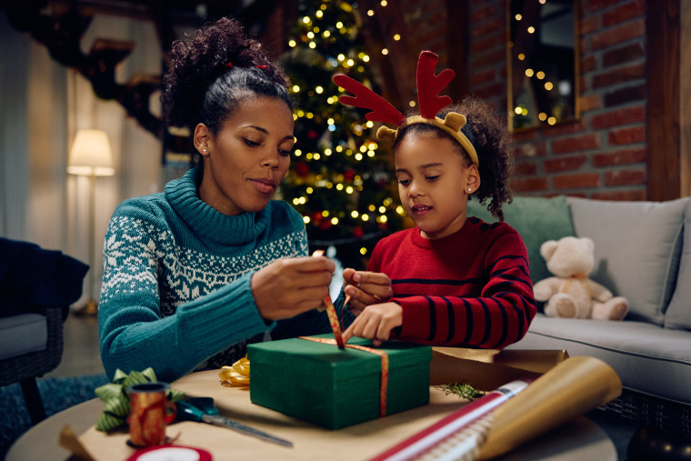 Black little girl assisting her mother in wrapping gifts 