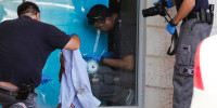 Police inspect a bullet hole through a glass window and bloody articles of clothing outside