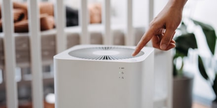 Close up hand of a mother turning on home air purifier for her newborn baby who is sleeping in the crib in the nursery. Fresh air. Cleaning and removing dust and bacteria. Healthier life and living concept