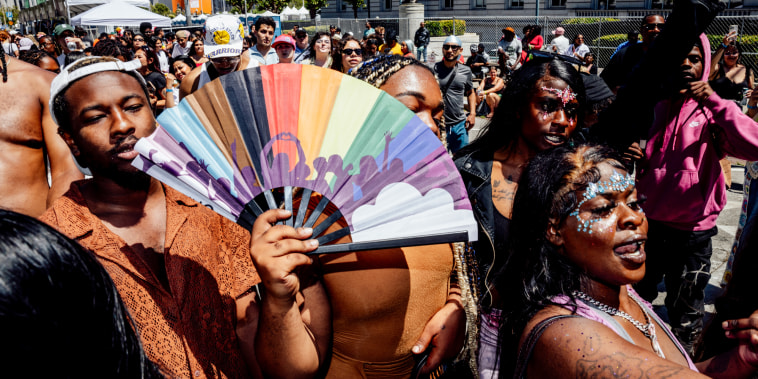 People dance and someone holds a rainbow hand fan outside during an event