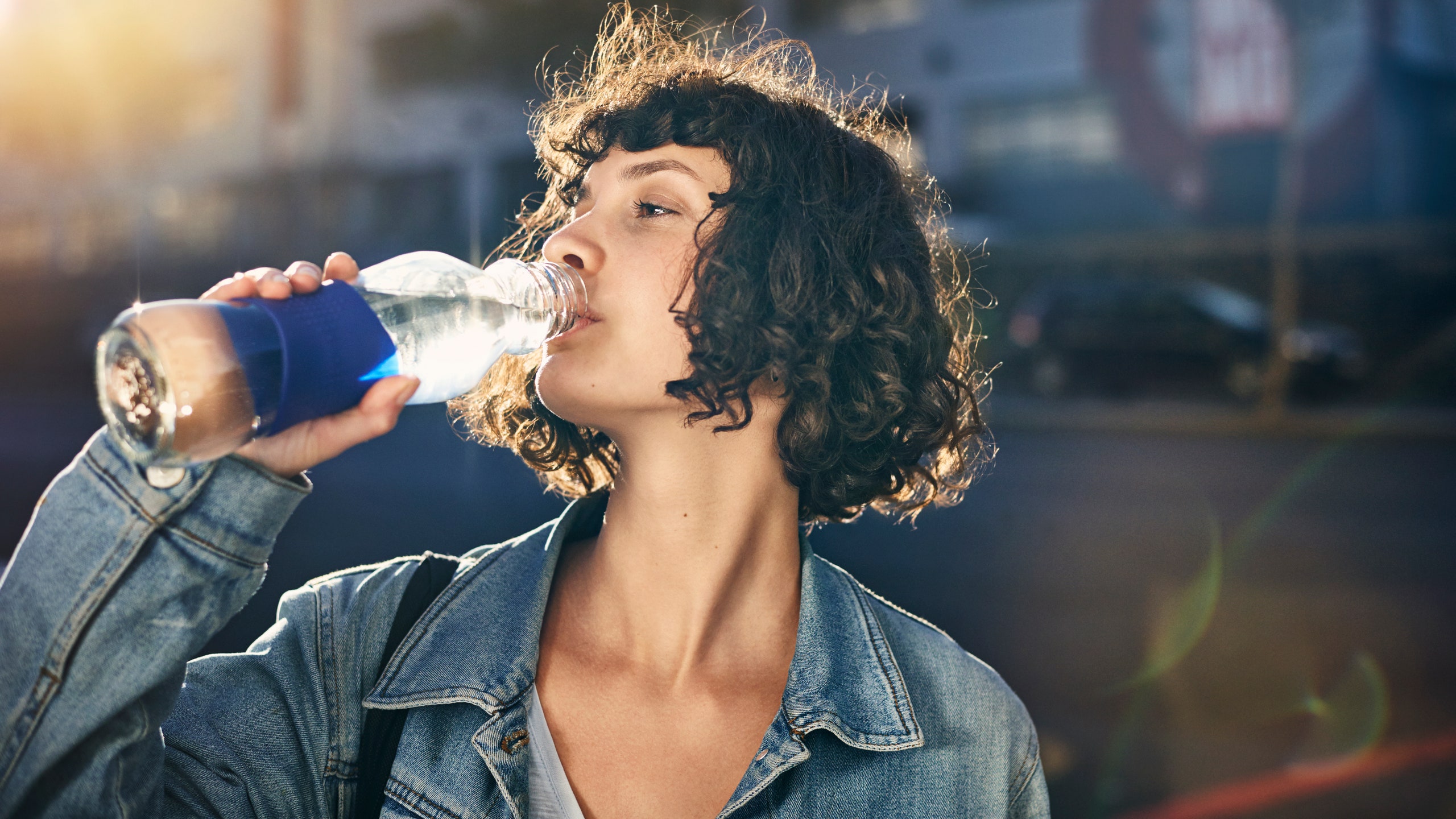 Woman with curly bob haircut drinking water outside