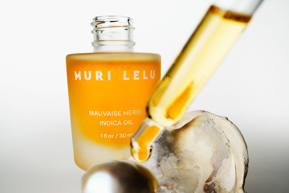 photo of bottle of orange Muri Lelu Facial Oil with dropper dropping on pearl and oyster shell on gray background