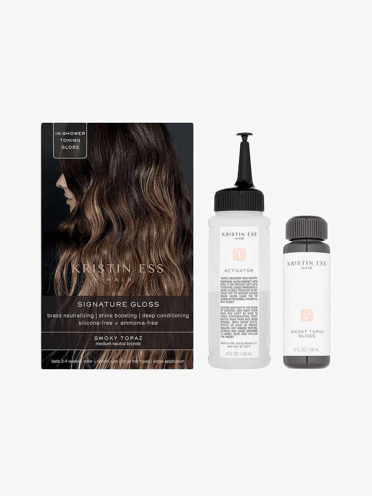 Kristin Ess Signature Hair Gloss in branded amber and clear bottles with black caps next to branded box packaging on light gray background