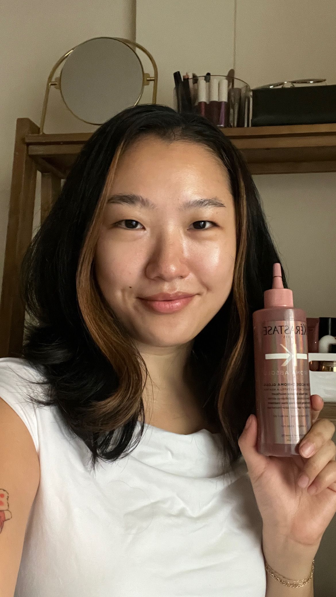 A selfie of Sarah Han holding a bottle of Krastase Chroma Absolu Soin Acide Chroma Gloss with shiny hair