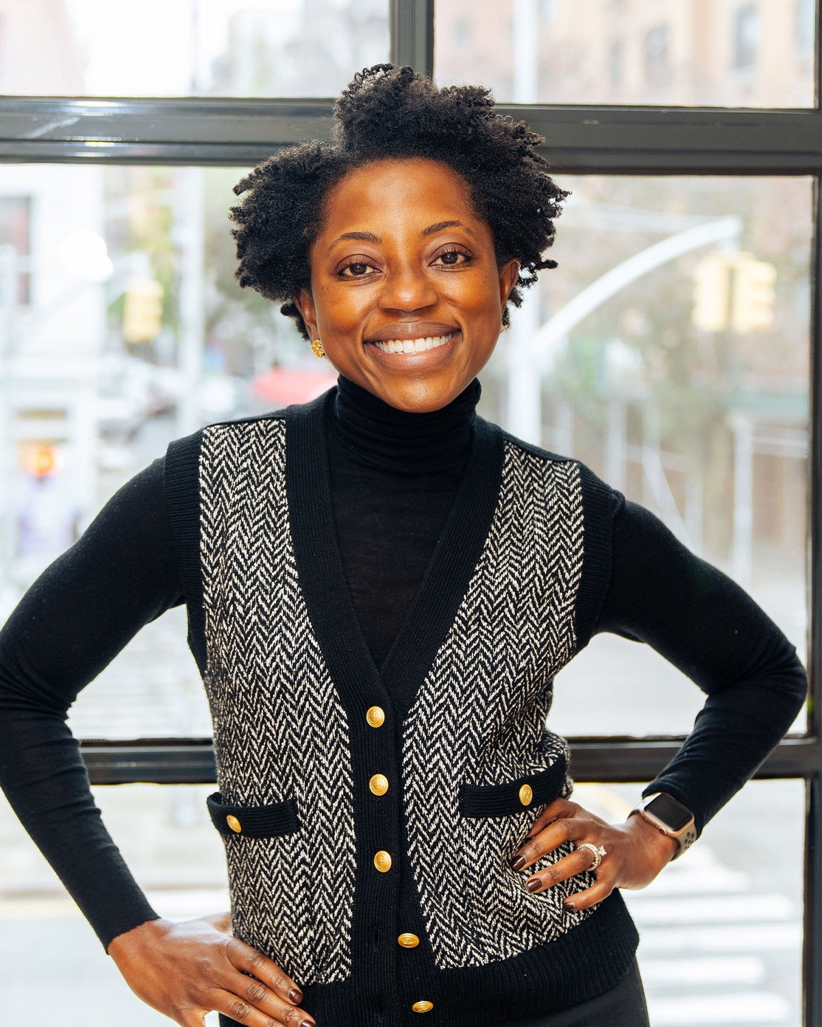 Dermatologist Naana Boakye shown standing in front of a window wearing a black and white herringbone vest with gold...