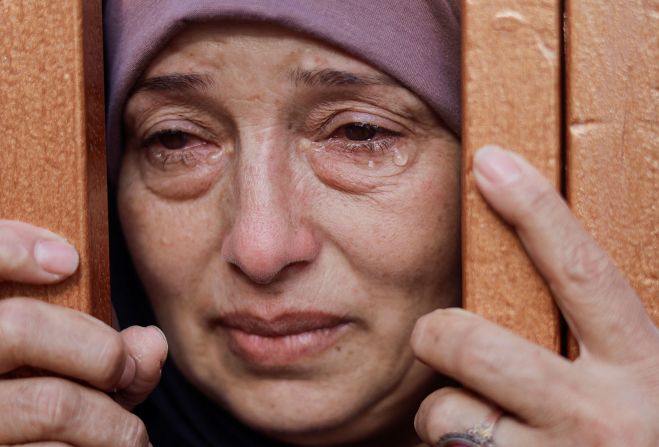 A woman looks from behind a gate at the bodies of Palestinians killed by Israeli strikes at a hospital in Khan Younis, Gaza, on October 26.