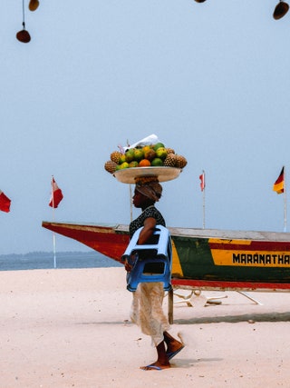 Woman on Ghanian beach carrying fruit on her head
