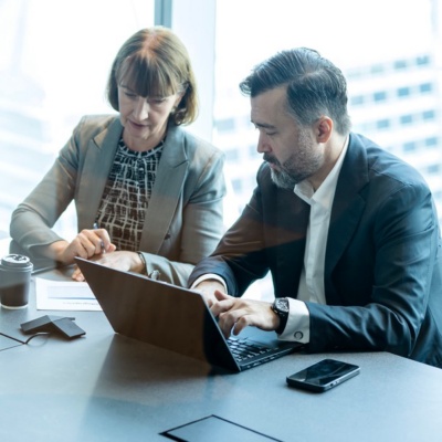 Two colleagues in a conference room referencing information on a laptop.