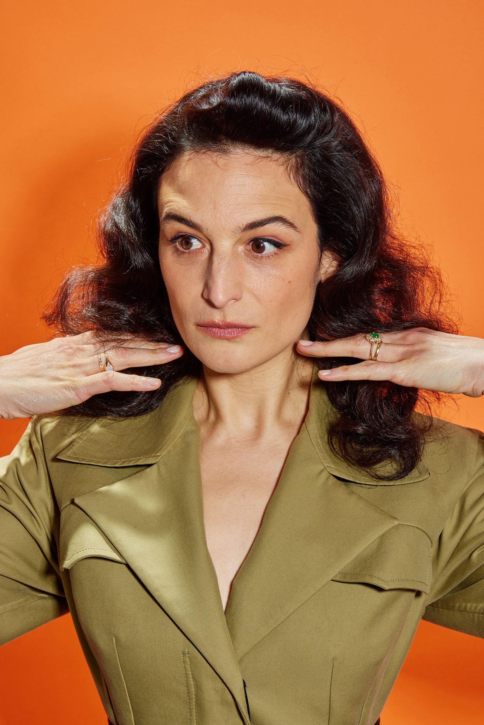 A portrait of the actor and comedian Jenny Slate with an orange background behind her.