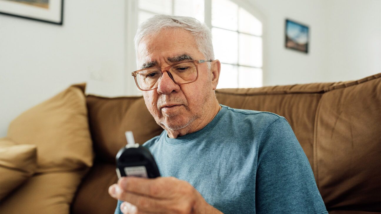 A man in blue shirt looks at a blood sugar monitor.