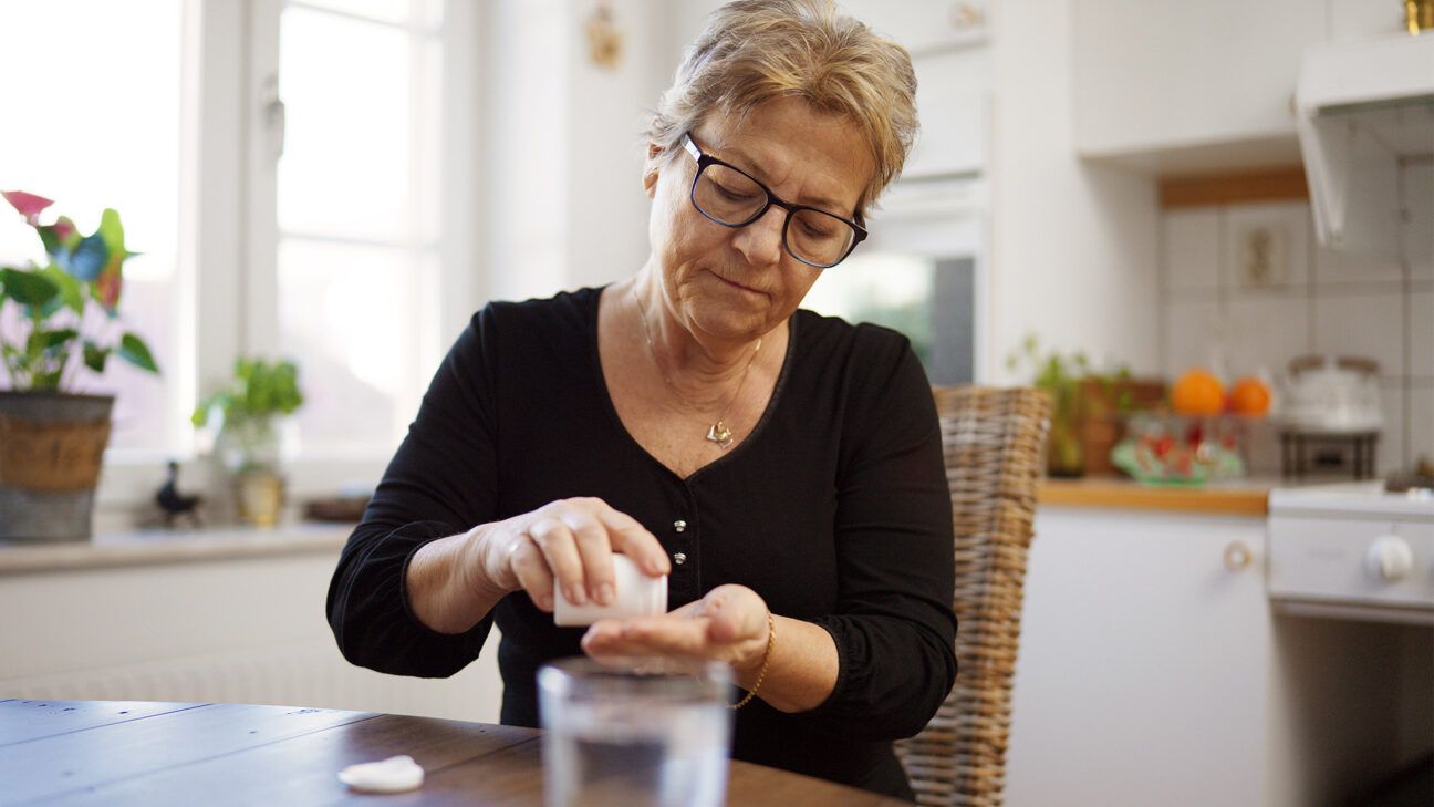 Woman in black shirt takes pills while sitting at a table.