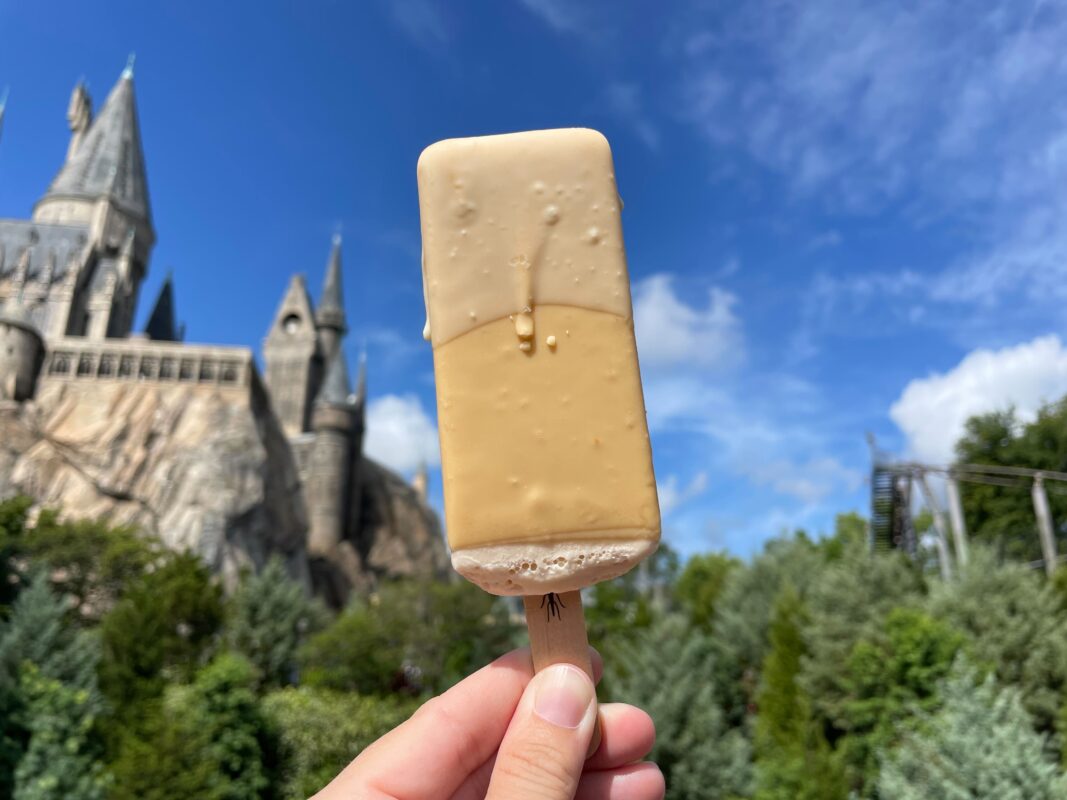 Butterbeer ice lolly held in front of Hogwarts Castle