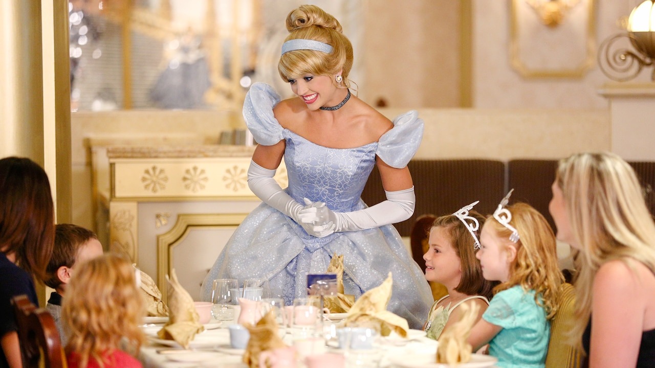 Princess Cinderella interacts with children sitting at a decorative dining table in a themed setting.