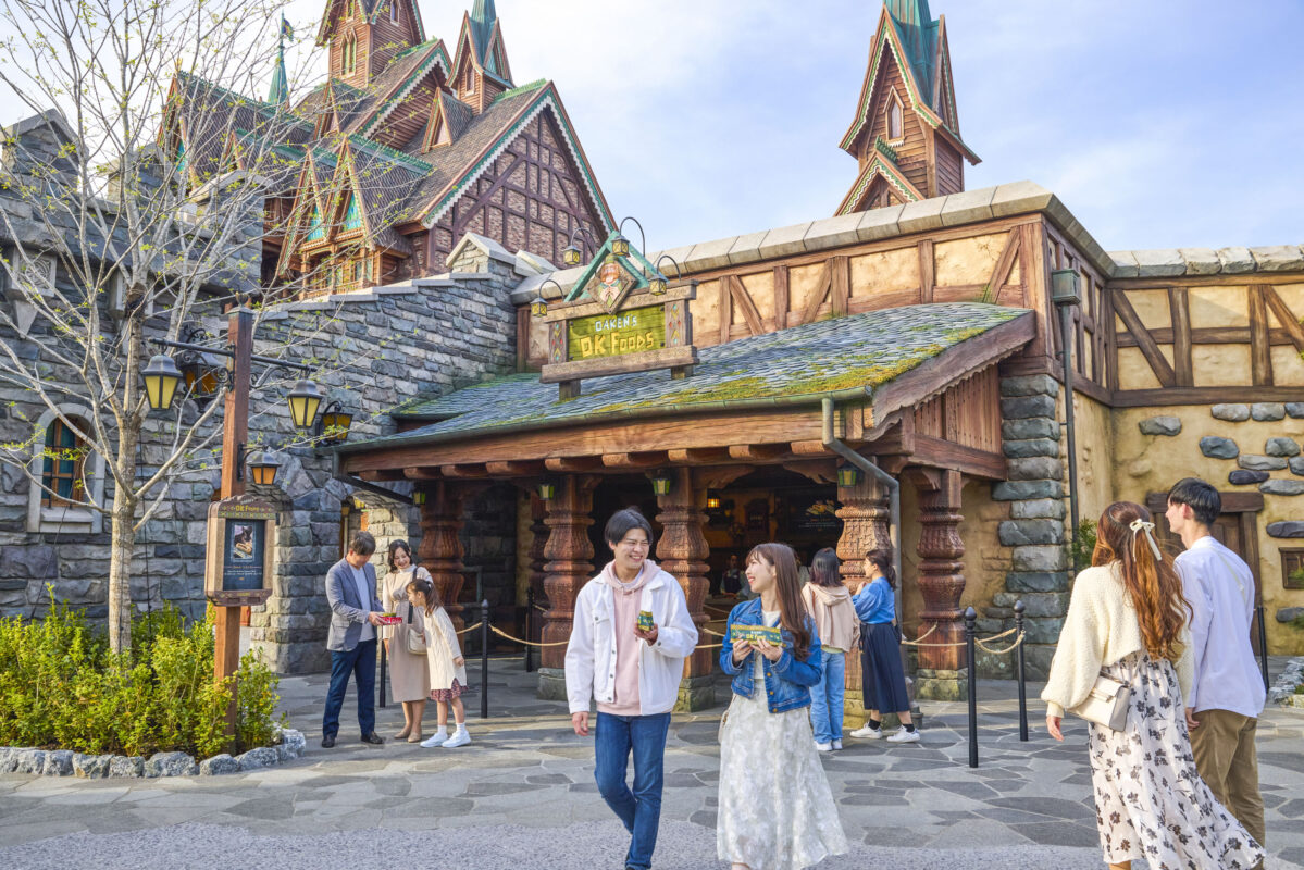 Visitors enjoying a sunny day outside a rustic, fantasy-themed restaurant in an amusement park.