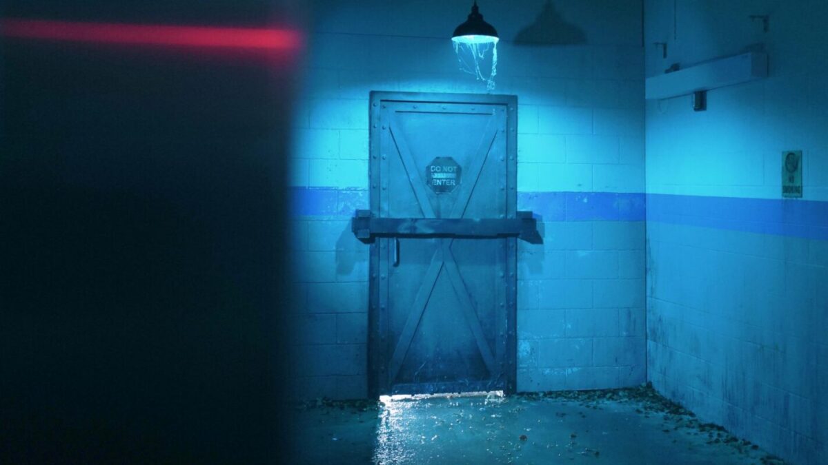 A dimly lit room with blue lighting, featuring water leaking from a ceiling vent onto a metal door labeled "Do Not Enter."