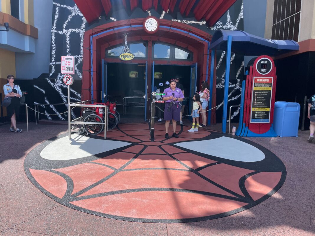 A theme park employee in a purple uniform stands by the entrance of The Amazing Adventures of Spider-Man