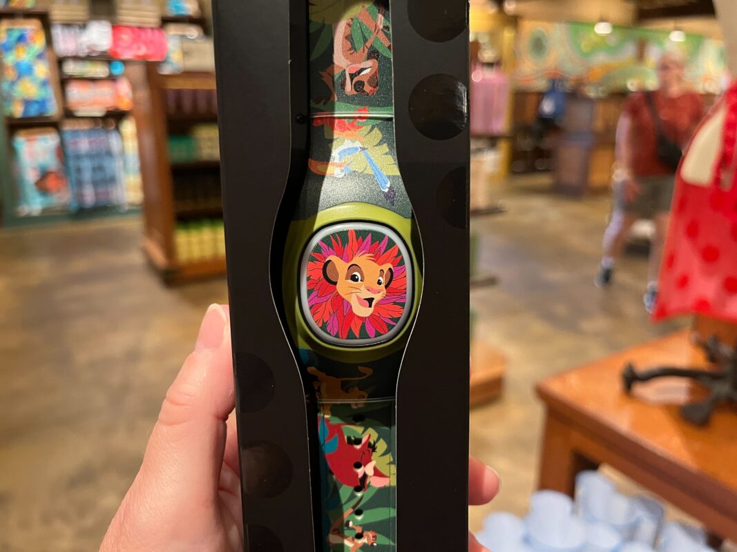 A hand holds a packaged watch featuring a cartoon lion face reminiscent of the Lion King and a colorful band, on display in Disney's Animal Kingdom store.
