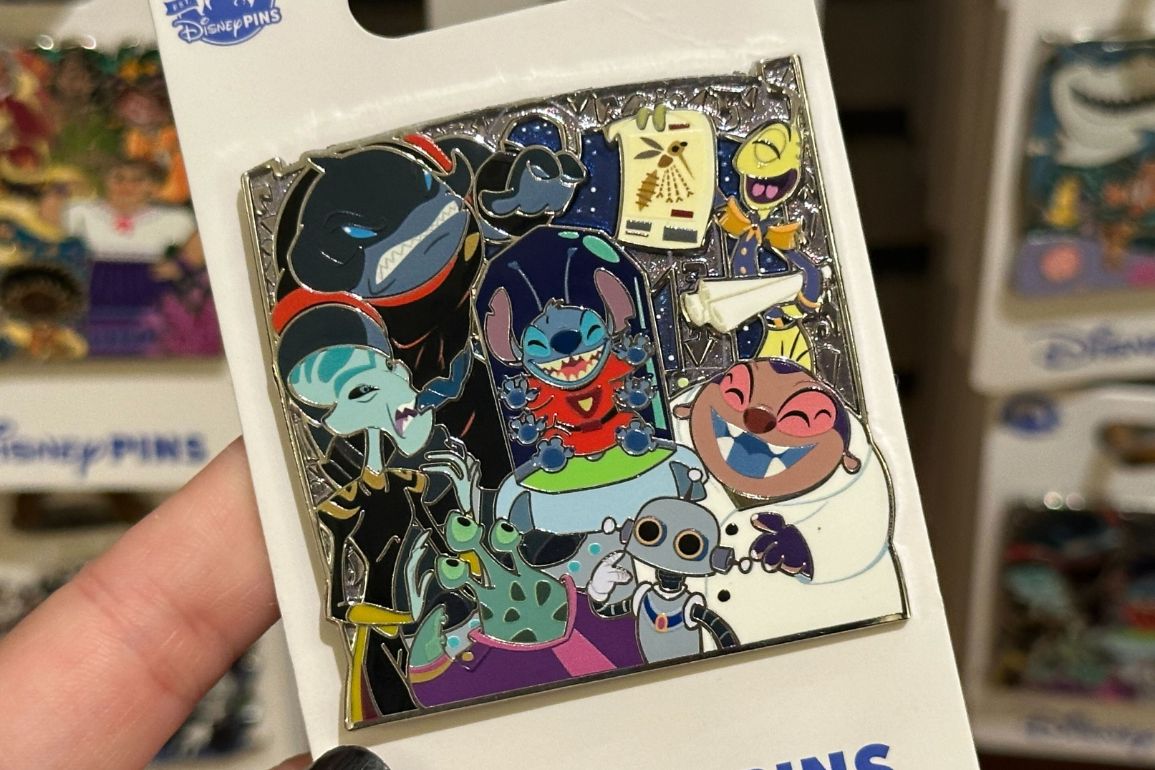 Hand holding a Disney pin featuring characters from "Lilo & Stitch" in various poses and outfits.