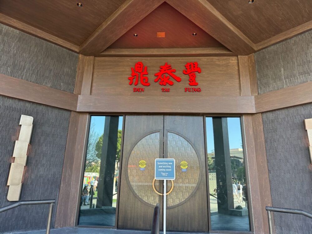 Restaurant entrance with large circular double doors and a sign that reads "DIN TAI FUNG" in both English and Chinese characters. A smaller sign in front of the door mentions closure for dine-in.