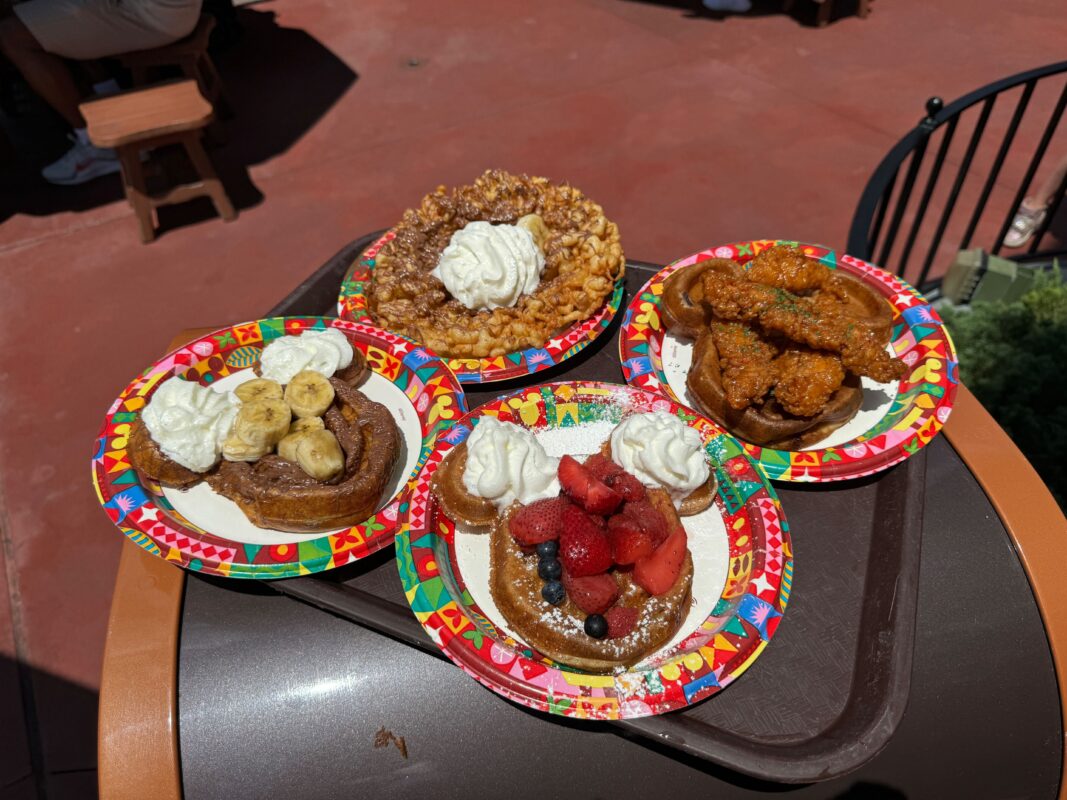 Four plates of food sit on a tray, reminiscent of the bountiful feasts from Sleepy Hollow. Each has distinct toppings: one with banana slices, one with whipped cream and mixed berries, one with fried chicken, and one with whipped cream and crumbled topping.