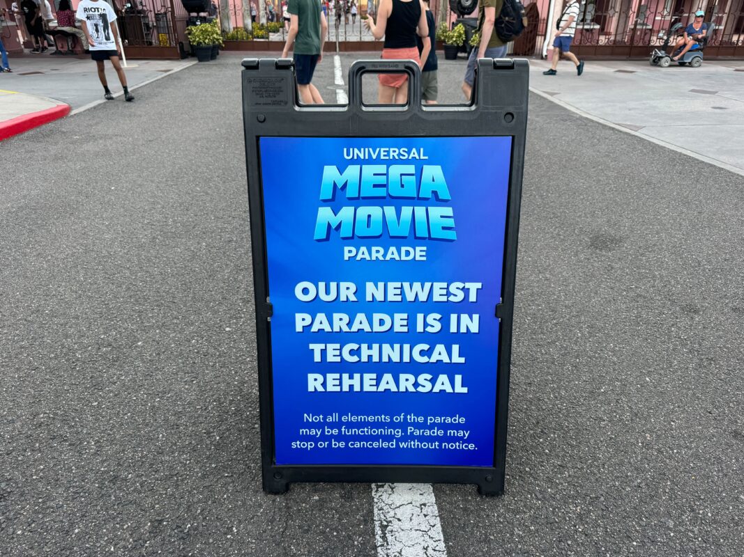 A sign reads: "Universal Mega Movie Parade. Our newest parade is in technical rehearsal. Not all elements of the parade may be functioning. Parade may stop or be canceled without notice.