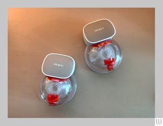 Aerial view of 2 breast pumps that are clear and circular with red internal parts attached to grey holder