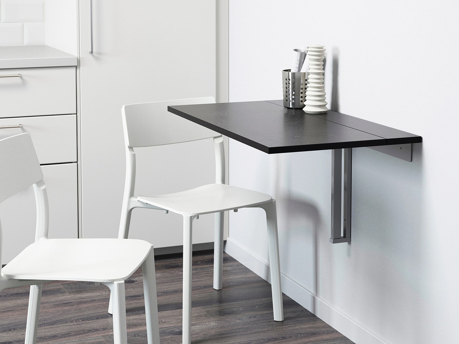 Small black shelf suspended from white wall with 2 white chairs surrounding it