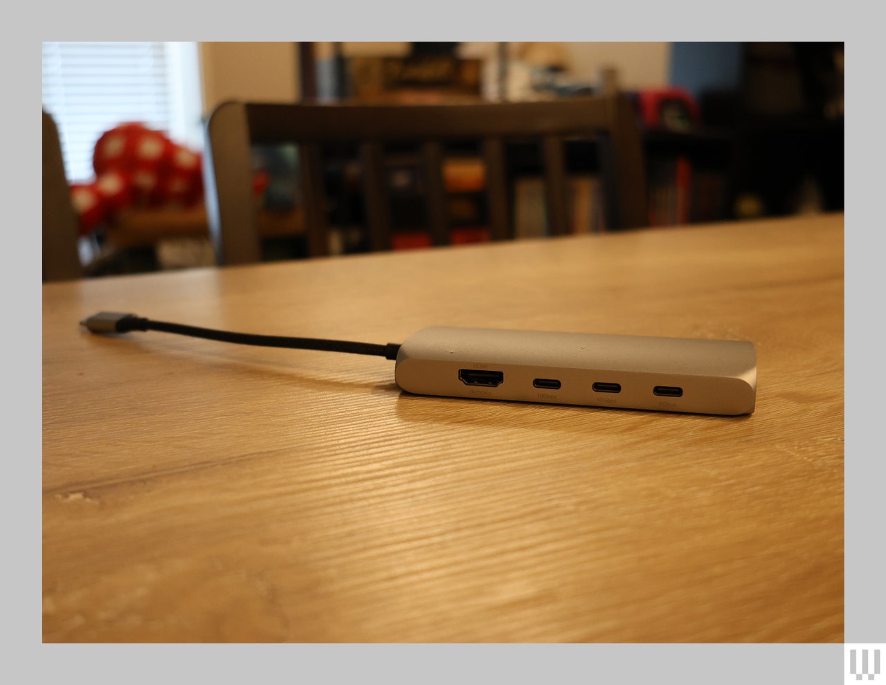 Silver rectangular electronic device with rounded edges, ports on the side, and a cord coming from the back