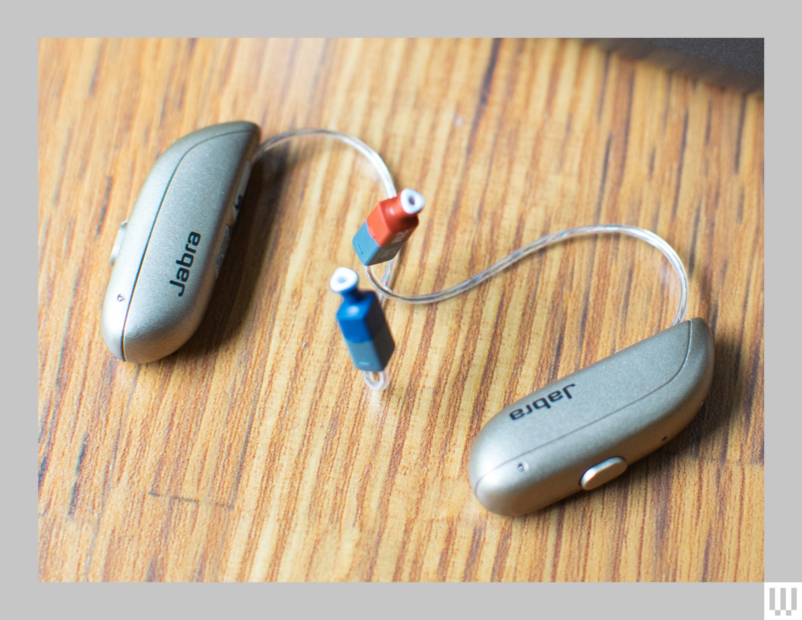 Close up of two silver behindtheear hearing aids on a wooden surface