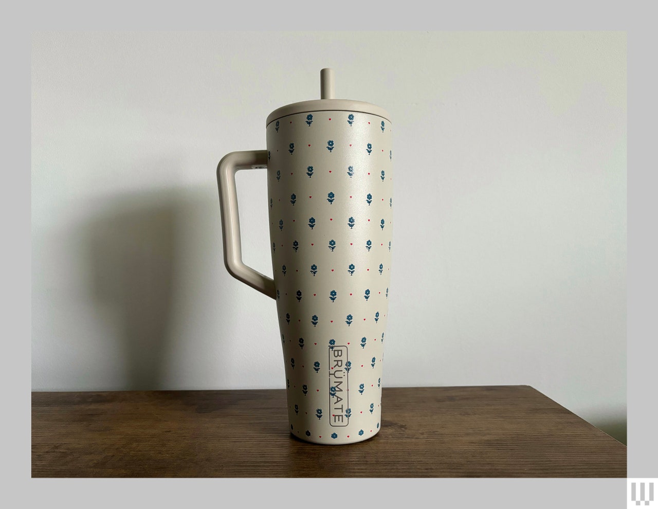 Tall beige reusable water bottle with narrow handle, floral pattern, and straw sticking out the top