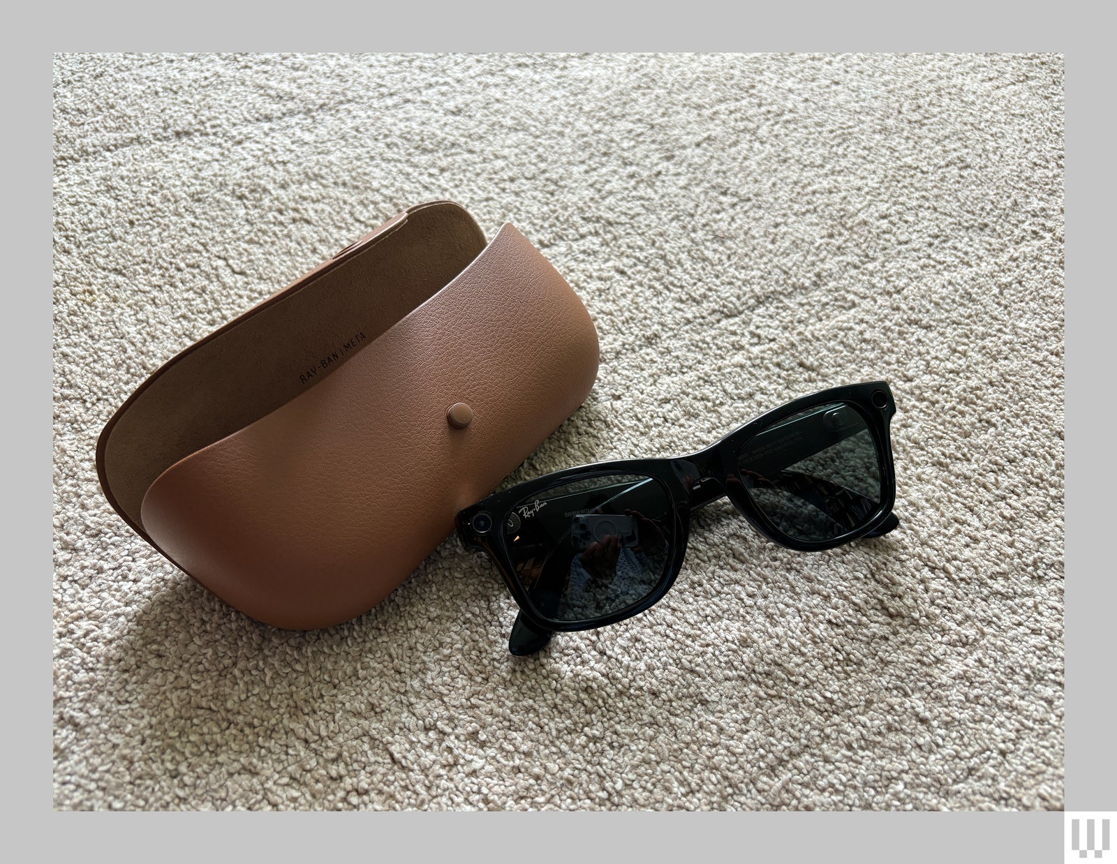 Black sunglasses beside a brown carrying case both sitting on a beige carpet