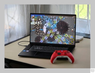 An open laptop with a video game on the screen and a red video game controller sitting beside it