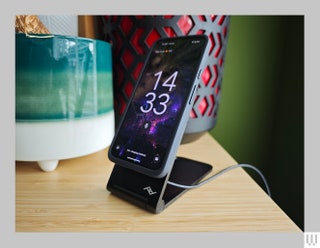 Black angular wireless phone charger propping up a phone near the edge of a table