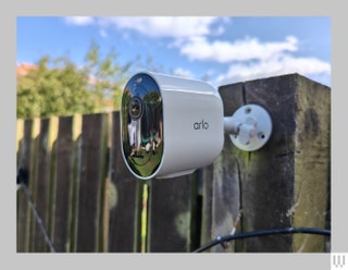 White ovalshaped outdoor security camera attached to wooden fence