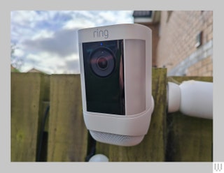 White rectangular outdoor security camera attached to wooden fence