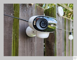 White ovalshaped outdoor security camera attached to wooden fence