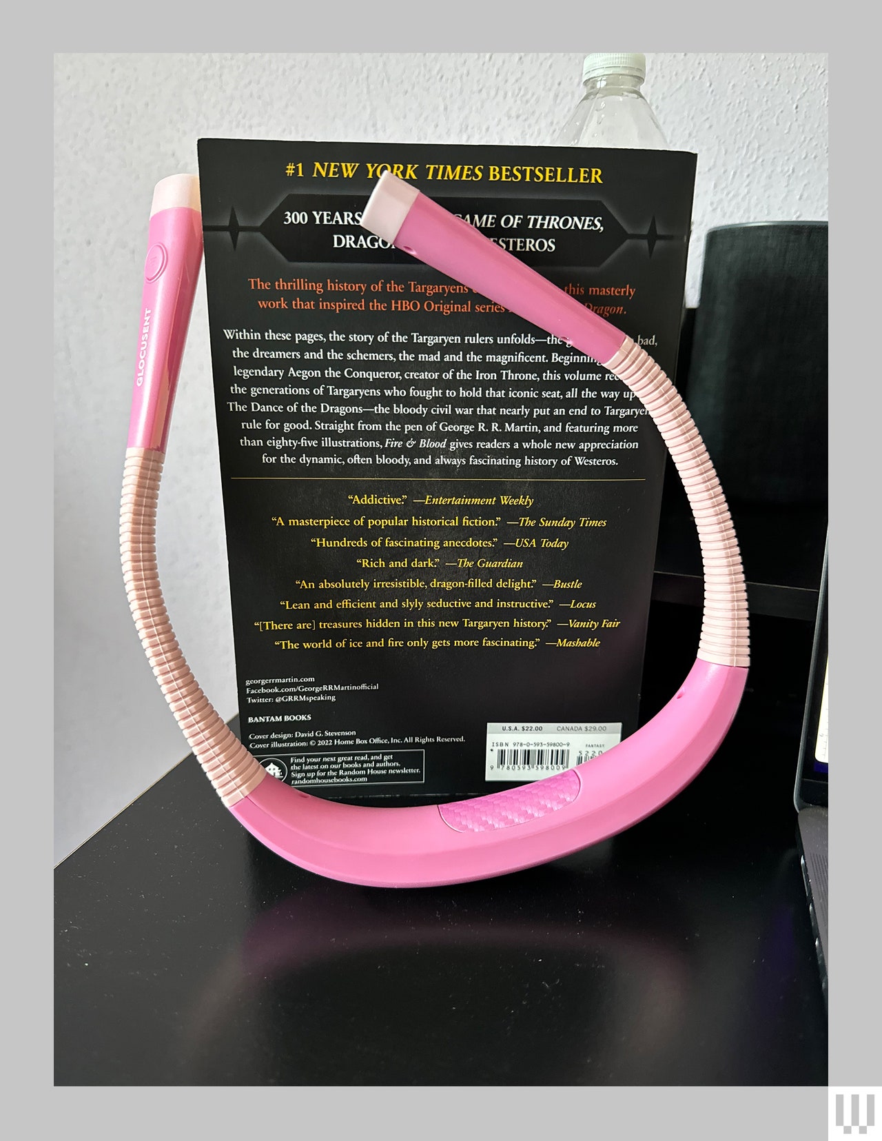 Curved u-shaped reading light that goes around the neck, leaning up against a book on a black surface