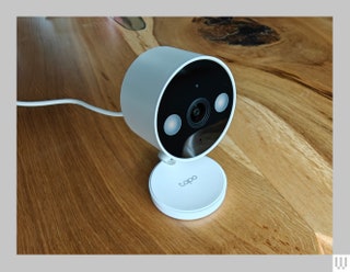 Small white security camera with a discshaped top and small circular base sitting on a wooden surface