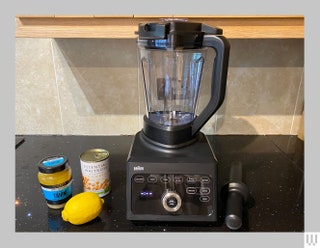 Black blender sitting on a black kitchen counter beside a jar a can and a lemon