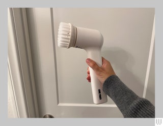 Hand holding up the Sonic Power Electric Scrubber a white circular brushhead with long handle