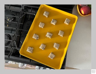 Great Jones Baking Sheet in yellow resting on the burners of a stove with squares of raw dough on top