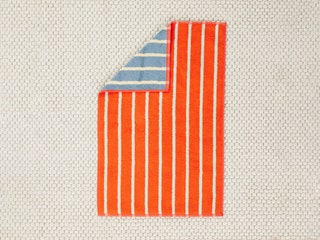 Dusen Dusen Towel with orange and white stripes on one side a corner folded down to reveal blue and white stripes on the...