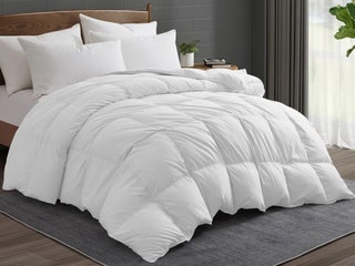 White Noise Goose Down and Feather All Season Comforter a white padded blanket draped on a bed with a grey rug...