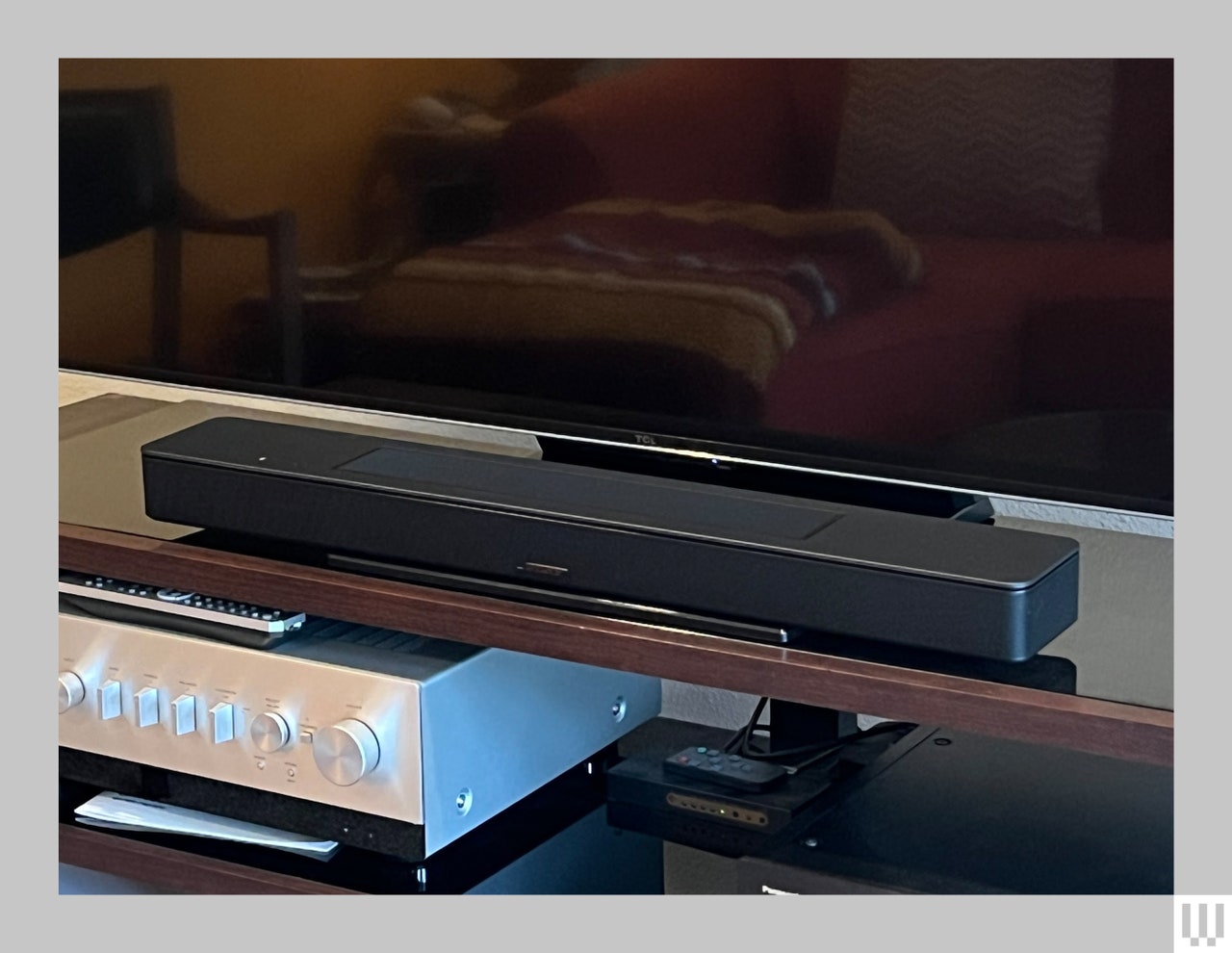 Bose Smart Soundbar, a long narrow black device, sitting at the base of a large flatscreen tv