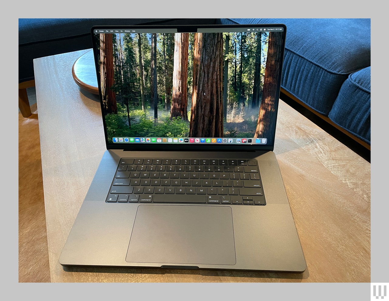 Front view of an open Apple MacBook Pro 16-inch 2024 edition, a slim dark silver laptop with large screen, keyboard and touchpad showing a forest scene on the screen